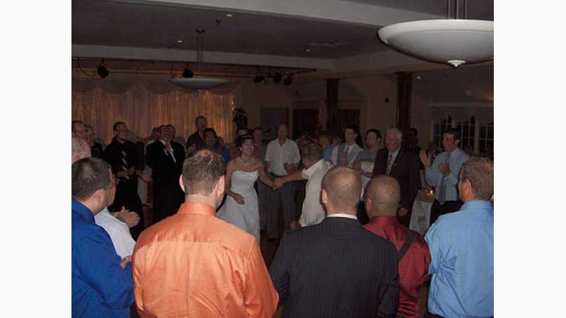 From wedding 4, Ancaster DJ, Bride in lovely white gown dancing with guest surrounded by guests all in a larger circle around them. Bride has a huge smile. Taken in Ancaster Ontario